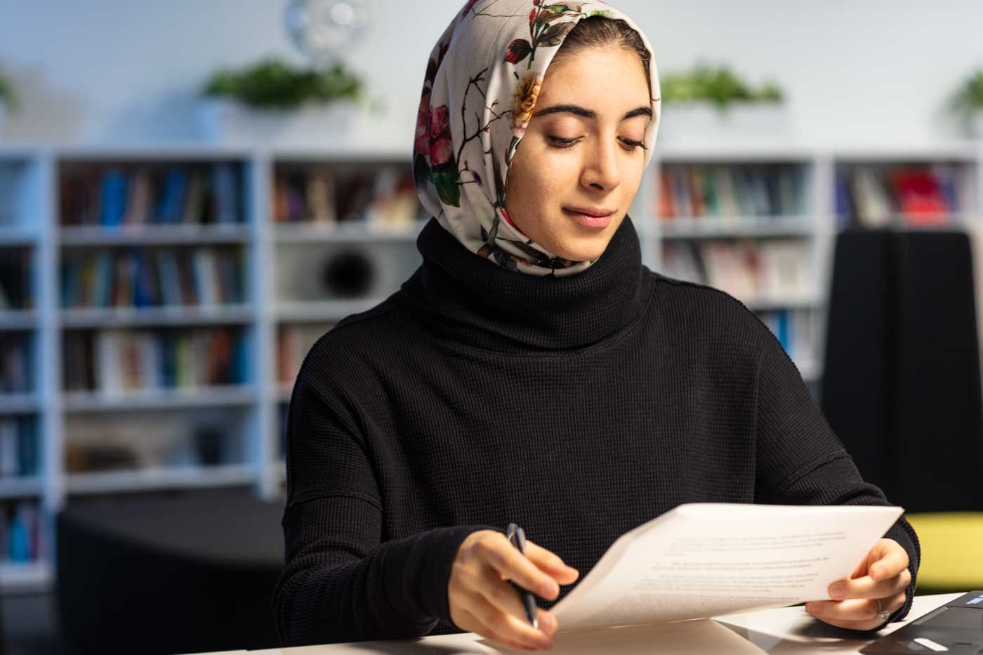 Woman sitting in library reviewing a document.