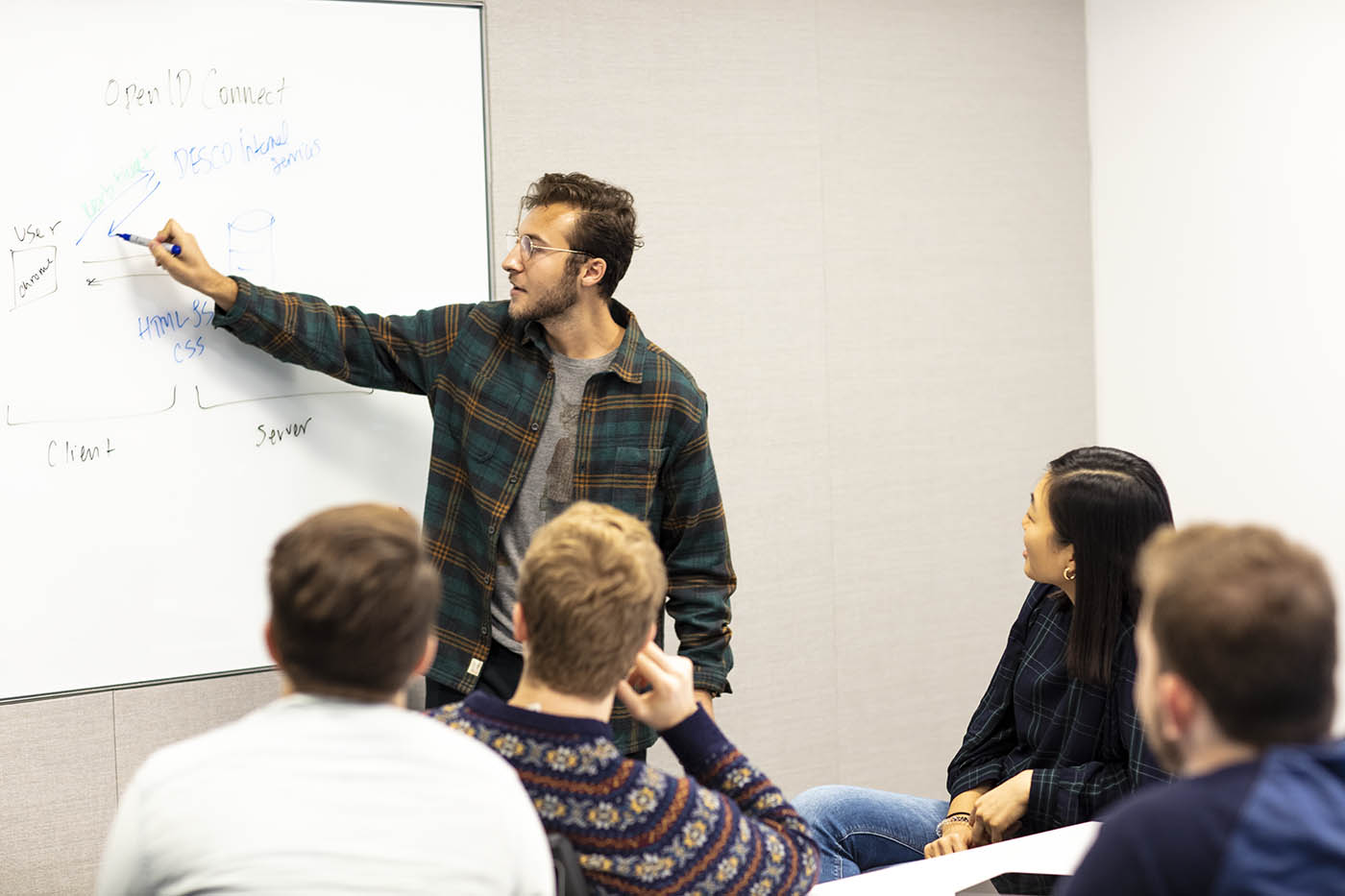 Man presenting at whiteboard to a small group of peers.